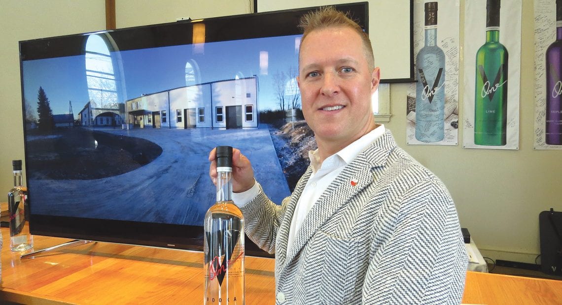 Paul Kozub stands in front of picture of his new distillery in Poland.