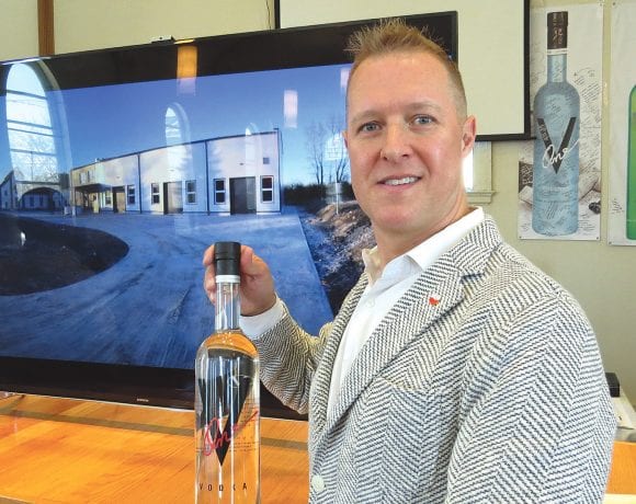 Paul Kozub stands in front of picture of his new distillery in Poland.